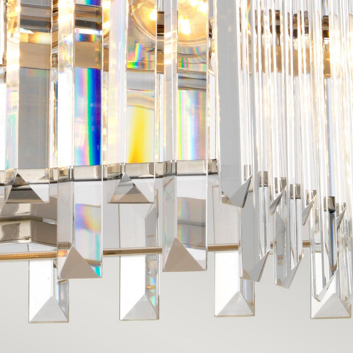 A close-up of the Aries 4 Light Small Chandelier in polished nickel showcases its numerous vertical, rectangular high-quality crystal prisms. These prisms refract light to create subtle rainbow reflections. Against a blurred background, the polished nickel accents emphasize the chandelier's elegance and intricate design elements.