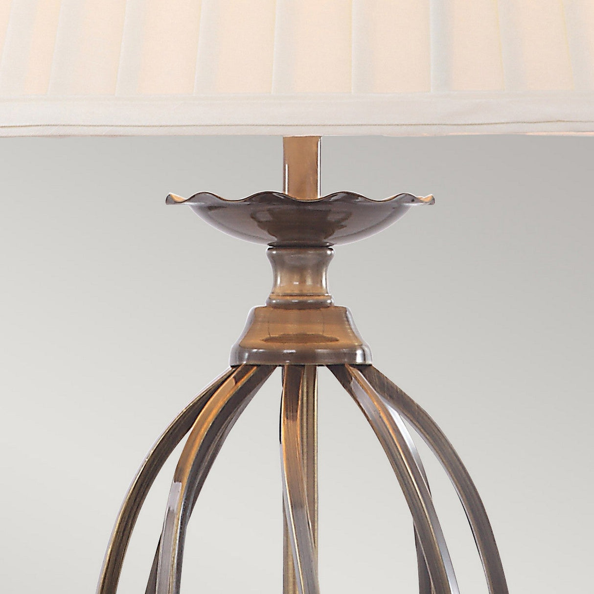 Close-up of the Artisan Table Lamp - Aged Brass, showcasing its pleated white shade and intricately designed base. Curved metal strips create a symmetrical pattern against a soft gray background.