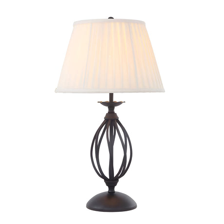 The Artisan Table Lamp - Black features a white pleated lampshade resting on an ornate base with a black finish, highlighting hand-formed metal scrolls in an intricate swirled cage design on its round pedestal.