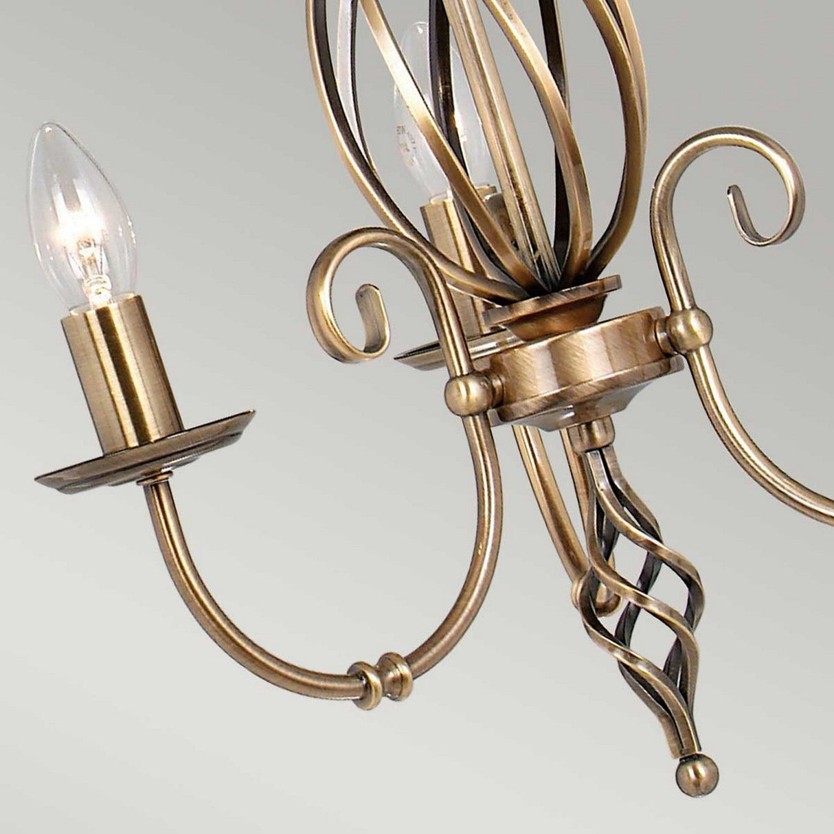 The Artisan 3 Light Chandelier in aged brass, featuring spiral arms with two exposed candle-like bulbs, adds a vintage touch against a light gray background.
