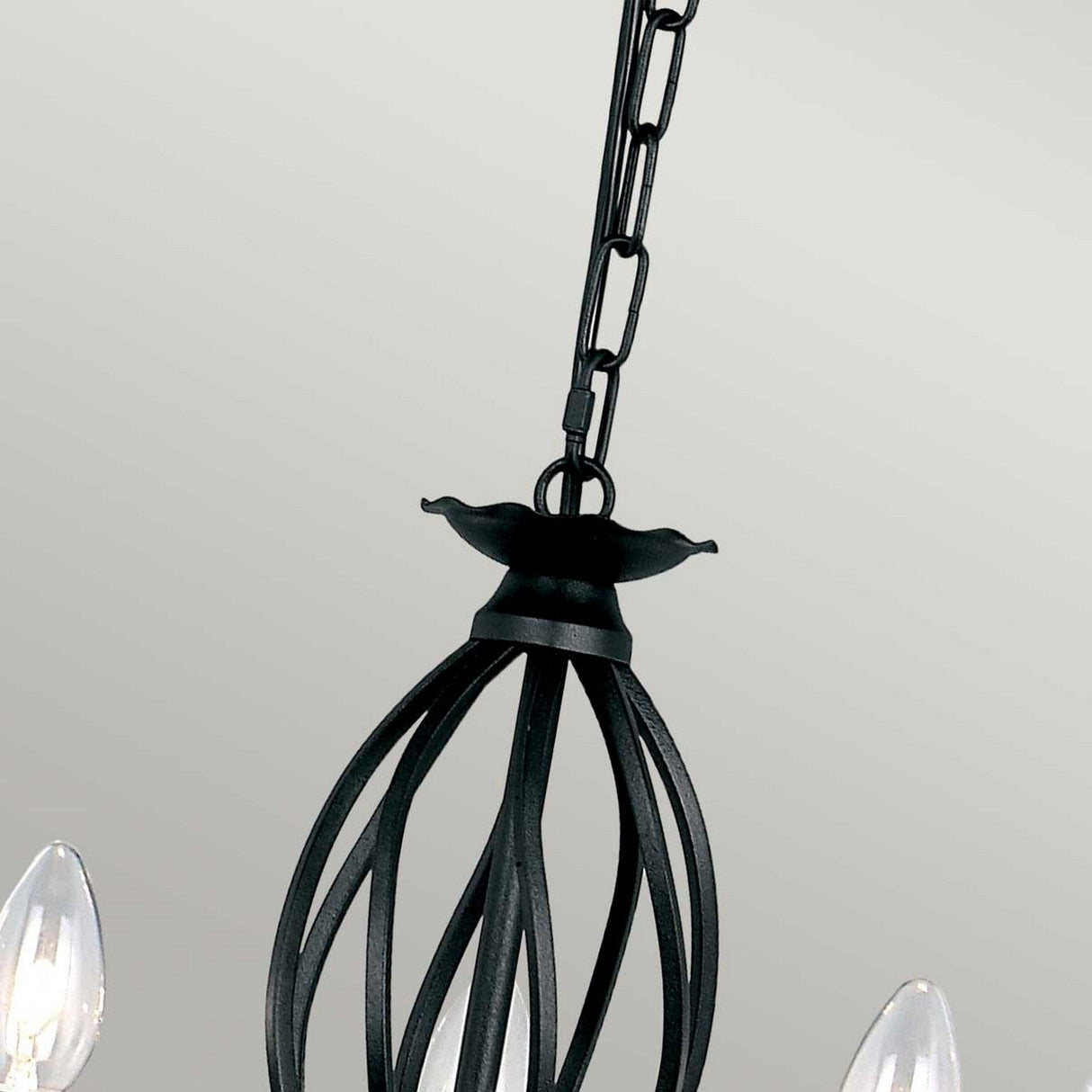 Close-up of the Artisan 5 Light Chandelier - Black, a stunning metal piece featuring hand-formed scrolls and a unique cage-like design. Suspended by a chain, it highlights candle-style bulbs set against a neutral background.