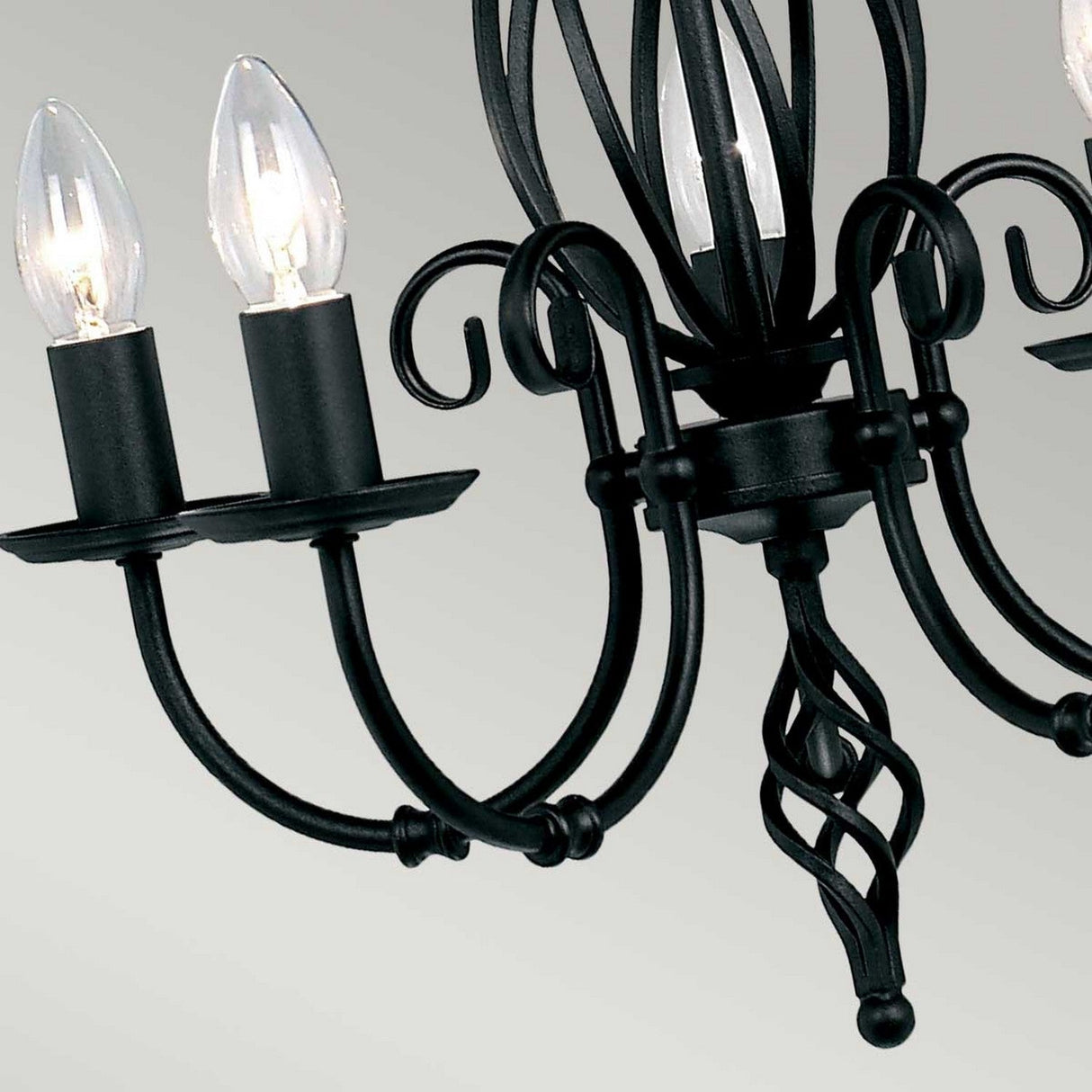 Close-up of the Artisan 5 Light Chandelier - Black, showcasing its twisted central stem. The chandelier includes three candle-shaped light bulbs mounted on gracefully curved arms. Its design is highlighted by elegant hand-formed scrolls, which contribute a classic touch.