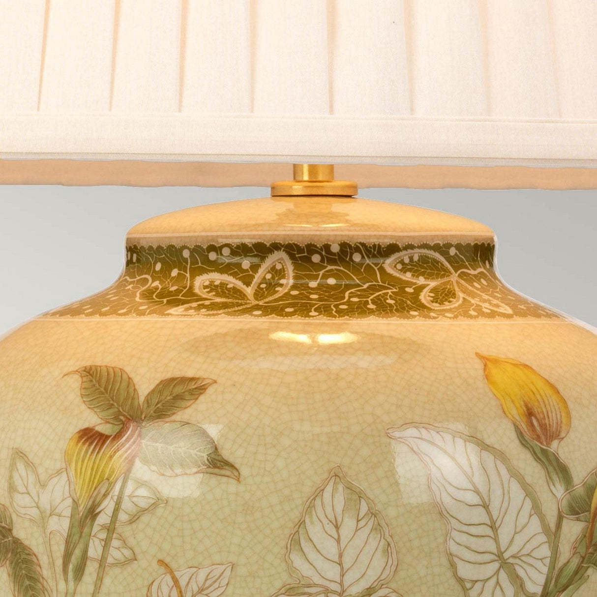 Close-up of the Arum Table Lamp - Aged Brass. The base showcases detailed yellow flowers and green leaves, evoking the style of Chinese porcelain, complemented by a band of intricate vine designs beneath the shade. Its cream-colored pleated shade enhances its elegance.