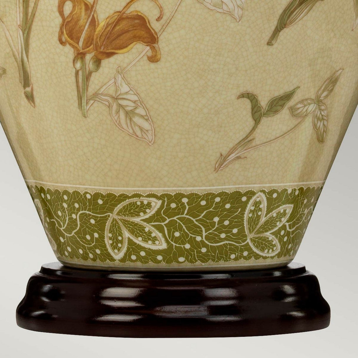 A close-up of an ornate Chinese porcelain vase with floral designs in muted colors shows the base featuring a green band adorned with white leaf patterns. It rests elegantly on a dark wooden stand beside the Arum Table Lamp in Aged Brass.