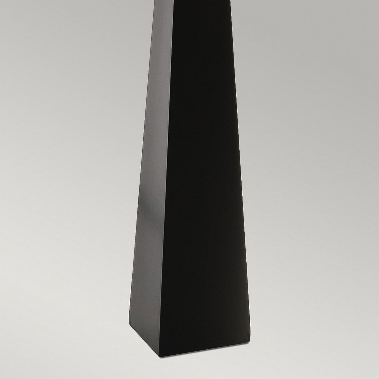 Against a light gray background stands the Ascent Floor Lamp with a sleek triangular prism design in black. This lamp combines the elegance of a decorative piece with modern functionality. Its simplicity and contemporary shape are accentuated by gentle lighting, casting subtle shadows.