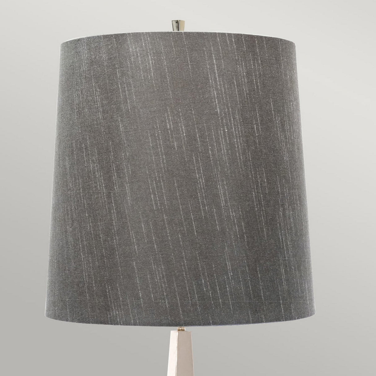 A close-up of a dark grey cylindrical fabric lampshade exudes modern elegance. The subtle texture with faint vertical lines complements the sophisticated ambiance of the Ascent Floor Lamp With Dark Grey Shade - Polished Nickel. The background is a soft, light grey color, enhancing the polished appeal.