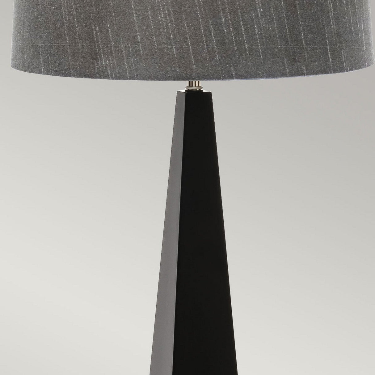 Introducing the Ascent Table Lamp - Black, an ideal addition to contemporary spaces. This modern lamp showcases a black, angular base complemented by a round, textured gray lampshade, forming a striking silhouette against a neutral backdrop. It's truly a minimalist masterpiece for any room.