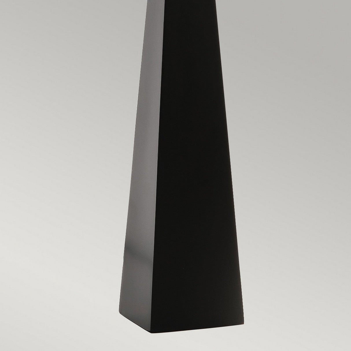 A tall, sleek Ascent Table Lamp in black, shaped like a triangular prism, stands vertically against a light gray background. Its smooth surfaces and sharp edges make it perfect for minimalist, contemporary spaces.