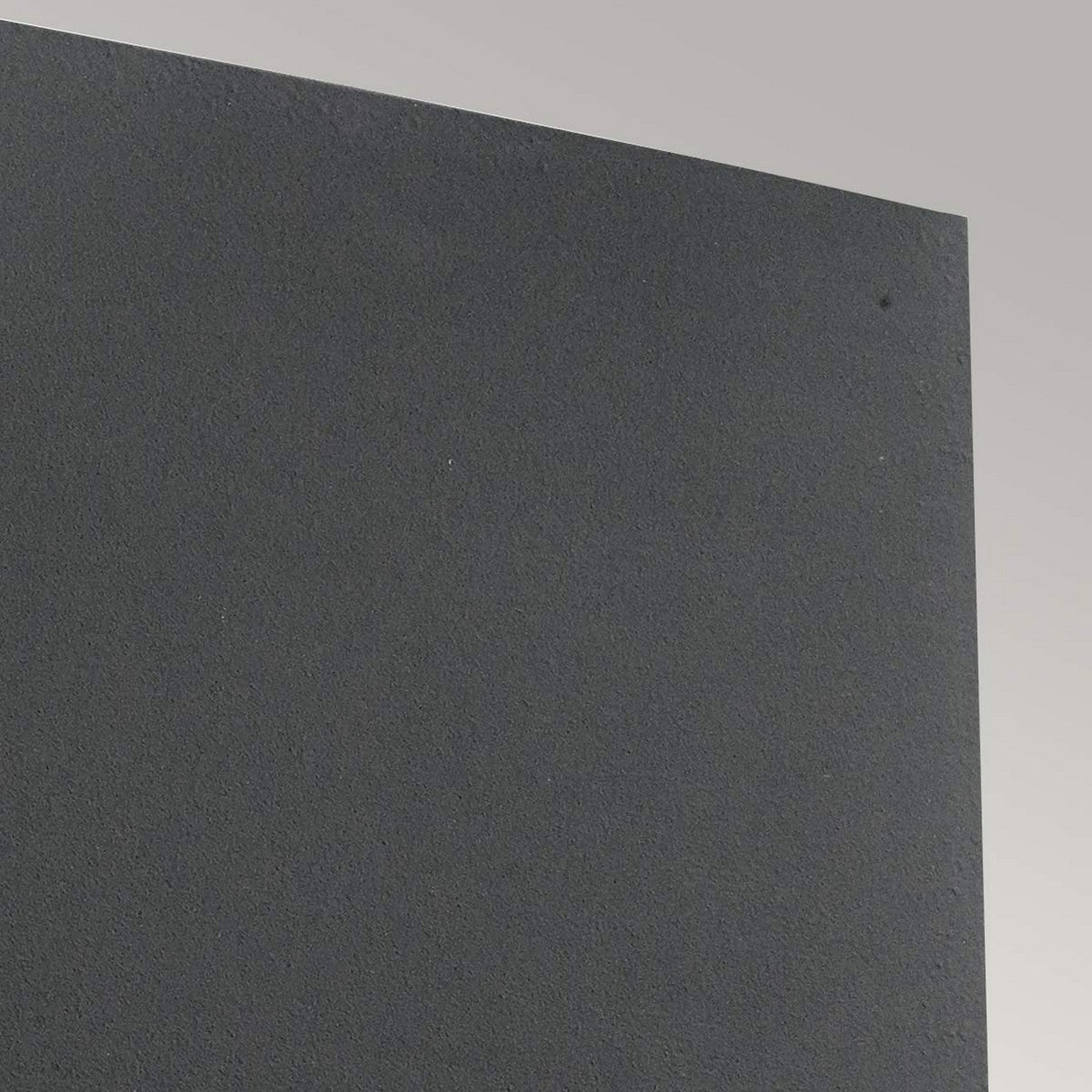 Close-up of a dark textured surface set against a light gray background, reminiscent of the Asker Outdoor 1 Light Up/Down - Graphite with its IP65 rating. The image highlights the intersection of smooth and rough areas, emphasizing the contrast between different materials or finishes, similar to how exterior lighting like this plays with shadows.