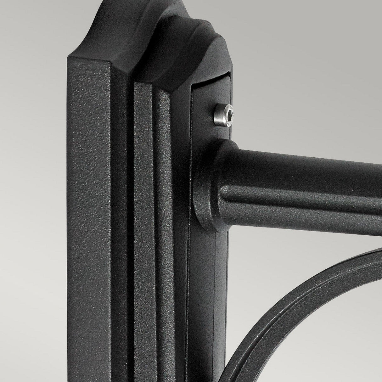 The image showcases a close-up of the Bologna Outdoor 1 Light Up Wall Light in black, featuring a metal bracket with a cylindrical rod attached to a rectangular frame. The surface is textured with visible screws, making it ideal for outdoor setups with an IP54 rating. The background is plain and light gray.