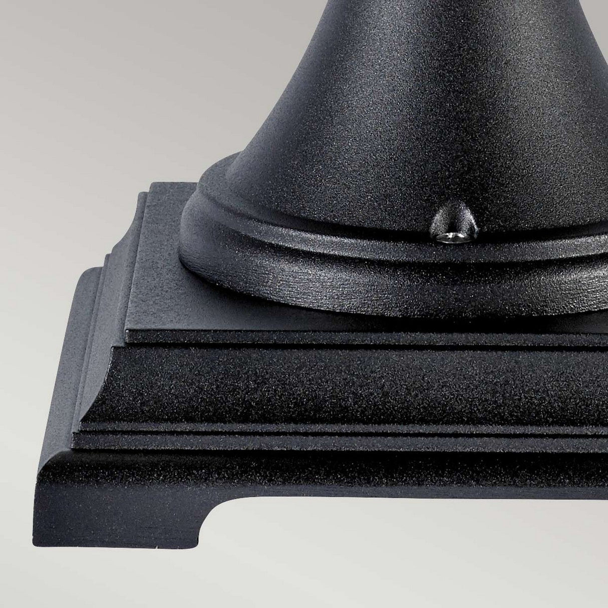 Close-up of the base of a Bologna 1 Light Pedestal - Black with its stepped layers and rounded detailing, set against a light gray background. This elegant piece of outdoor lighting embodies sophistication, perfect for enhancing any exterior space.