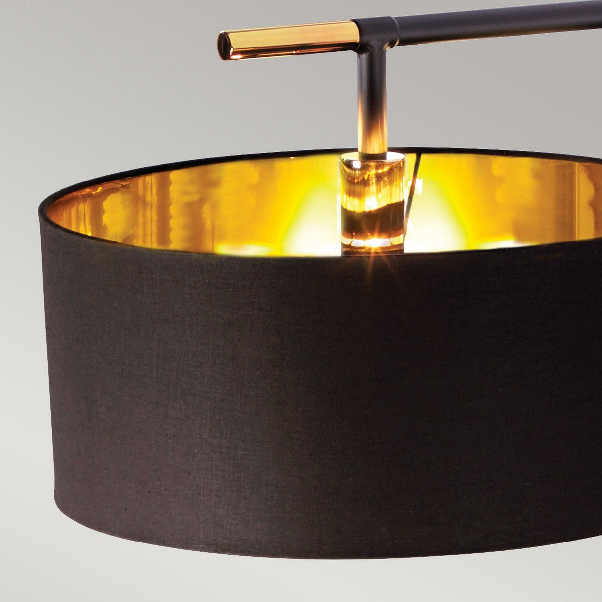 Close-up of the Balance Floor Lamp - Black/Polished Brass, highlighting its cylindrical lampshade with a black and polished brass exterior and a warm gold interior glow. The sleek horizontal rod above features gold accents, epitomizing modern design against the neutral background.