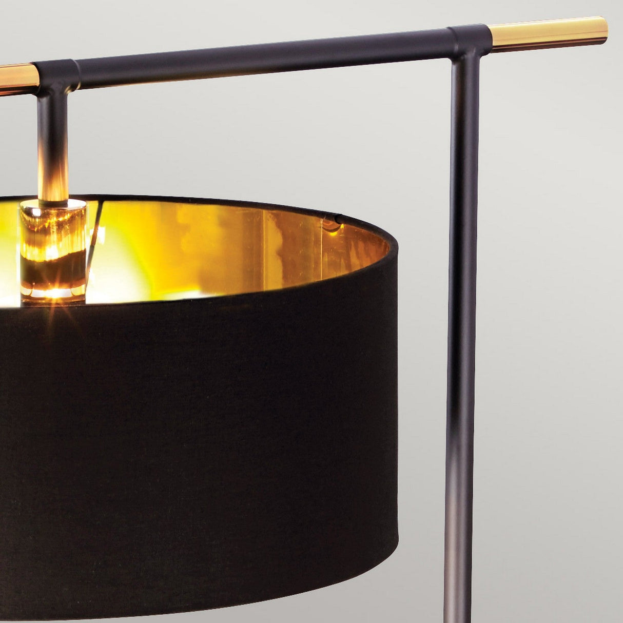 Close-up of the Balance Floor Lamp - Black/Polished Brass, showcasing a black cylindrical shade with a golden interior. The contemporary metal frame includes a horizontal bar on top, reminiscent of its signature style. The lamp emits a warm glow, accentuating the contrasting textures and colors of black and polished brass.