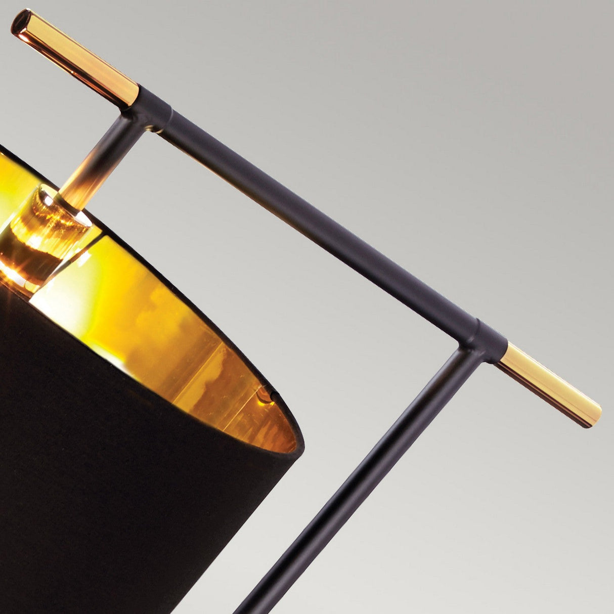 Close-up of the Balance Floor Lamp - Black/Polished Brass, featuring a modern design. This elegant piece highlights a cylindrical black shade with a gold reflective interior, supported by a minimalist frame with black and polished brass details. The background presents a neutral gray tone.