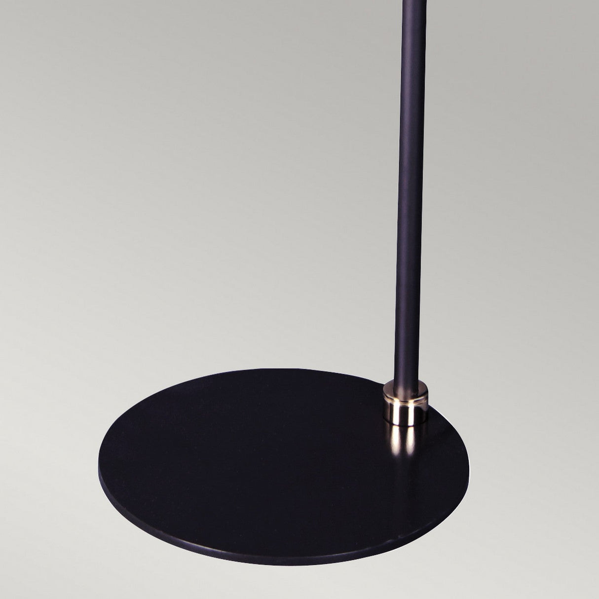 Close-up of the base of a Balance Floor Lamp - Black/Polished Nickel, showcasing its sleek circular metal foundation and vertical pole with an elegant polished nickel accent near the joint. This energy-efficient lighting fixture stands out remarkably against a neutral background, making it perfect for modern decor.