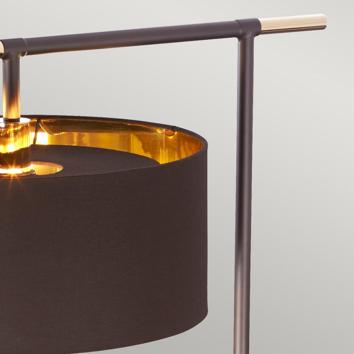 Close-up of the Balance Floor Lamp - Brown/Polished Brass showcasing a cylindrical black shade and a sleek metallic frame in polished brass. The gold interior of the shade provides a warm glow, enhanced by a subtle fabric diffuser, all set against a light gray background for a minimalist aesthetic.
