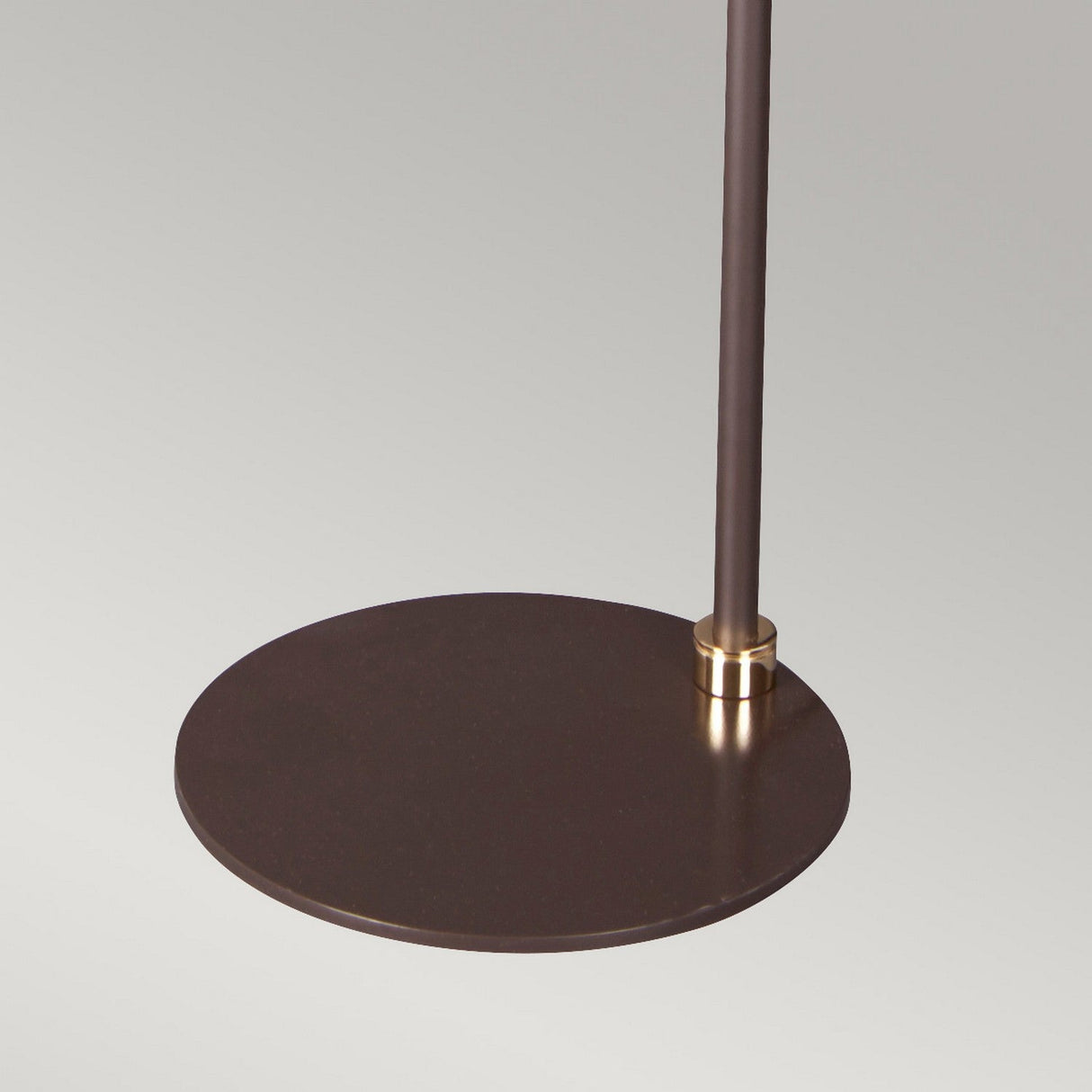 A close-up of the Balance Floor Lamp - Brown/Polished Brass base showcases a round, dark plate with a slim metal rod rising vertically. The rod is accentuated by a polished brass collar and set against a neutral background.
