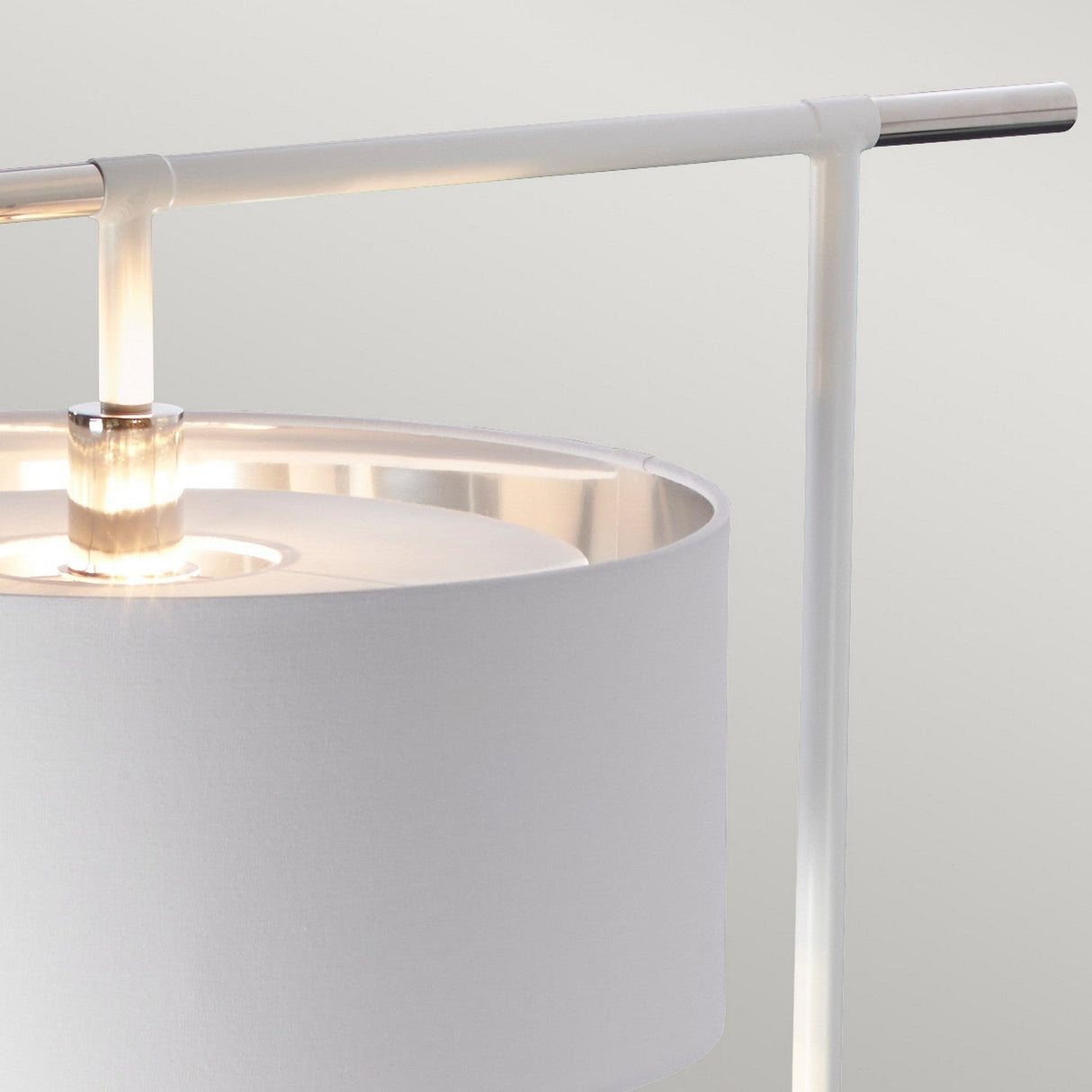 Close-up of a contemporary lighting piece featuring the Balance Floor Lamp with a white cylindrical shade and polished nickel stand. The lamp is lit, casting a soft glow around the top edge of the shade against a neutral, light gray background.