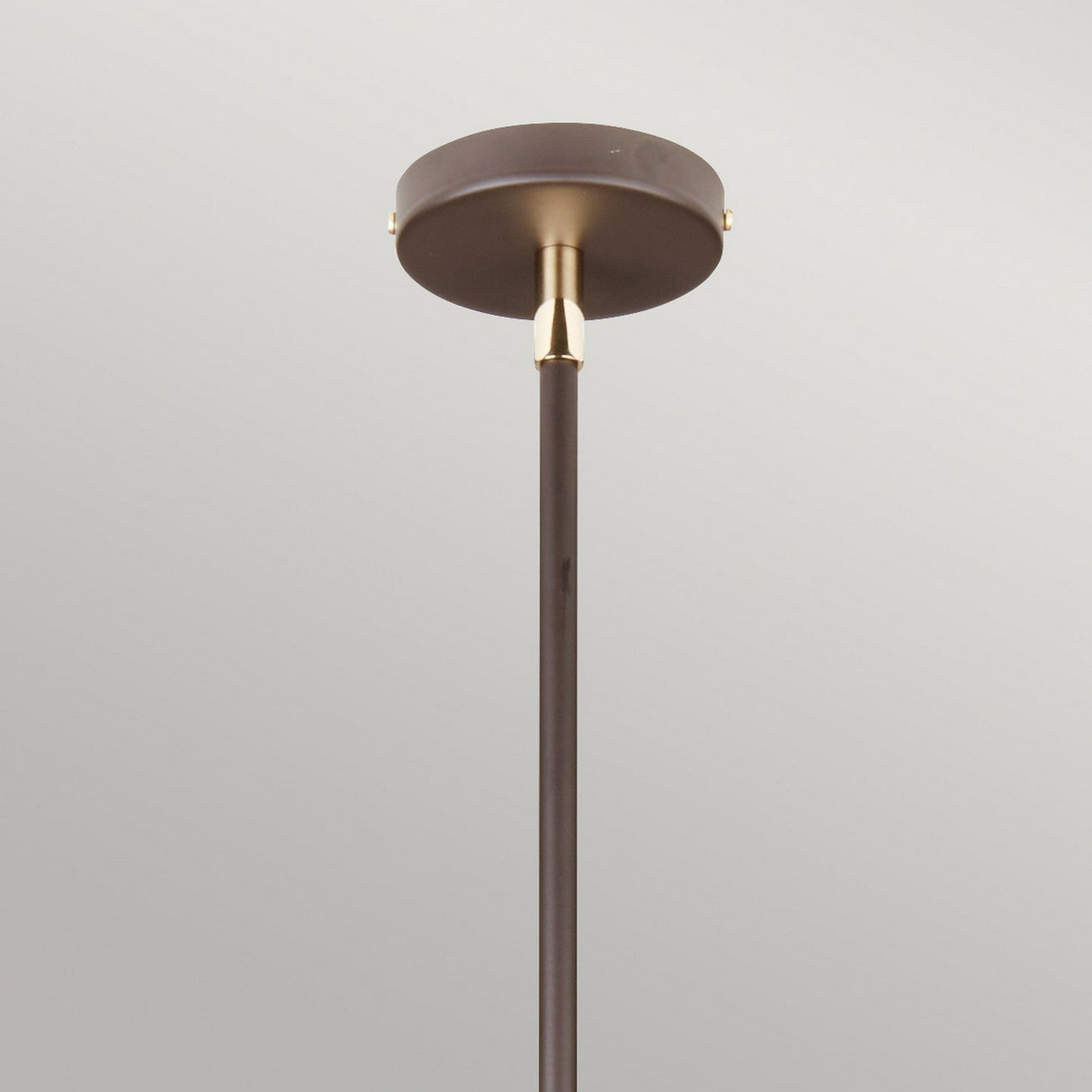 The Balance Pendant Light - Brown/Polished Brass boasts a bronze ceiling canopy and a slender downrod, beautifully completed with a polished brass fitting. Mounted against a plain grey wall, this fixture provides energy-efficient lighting enveloped in timeless elegance.