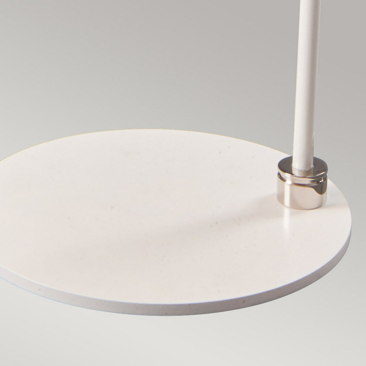 A close-up of the Balance 1 Light Table Lamp in White and Polished Nickel shows it elegantly resting on a sleek, modern circular white side table with a thin vertical metal support. The surface looks smooth and minimalist against a neutral backdrop.