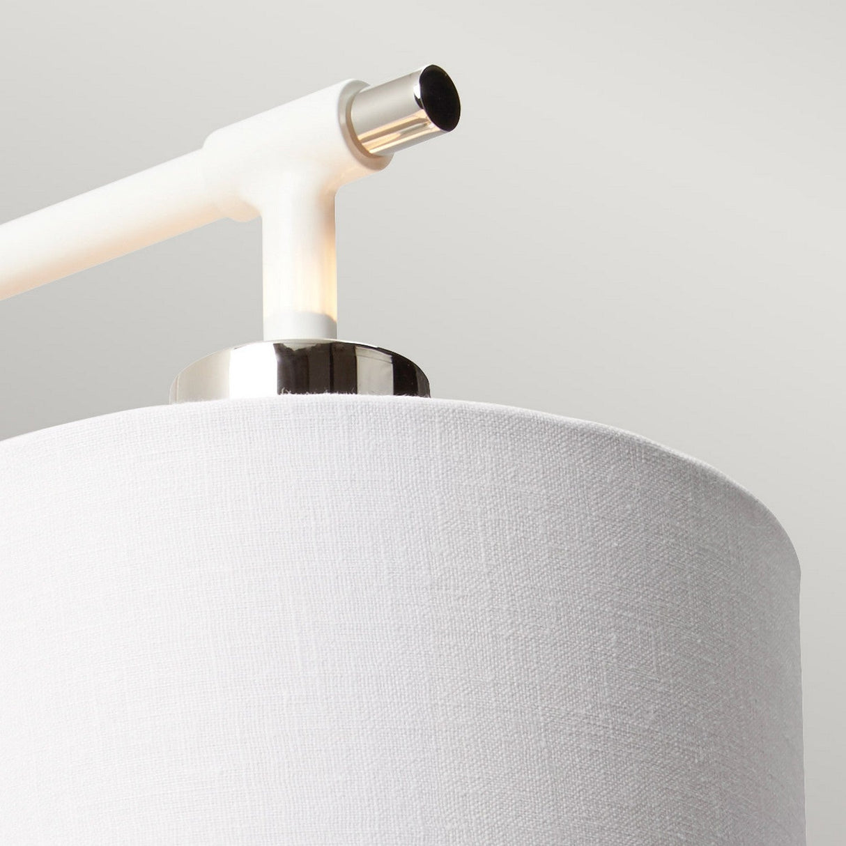 Close-up of the Balance 1 Light Wall Light, boasting a cylindrical white fabric shade with sleek polished nickel accents. Its clean design, enhanced by an energy-efficient lighting system, is highlighted by a white arm connecting to the shade against a neutral background.