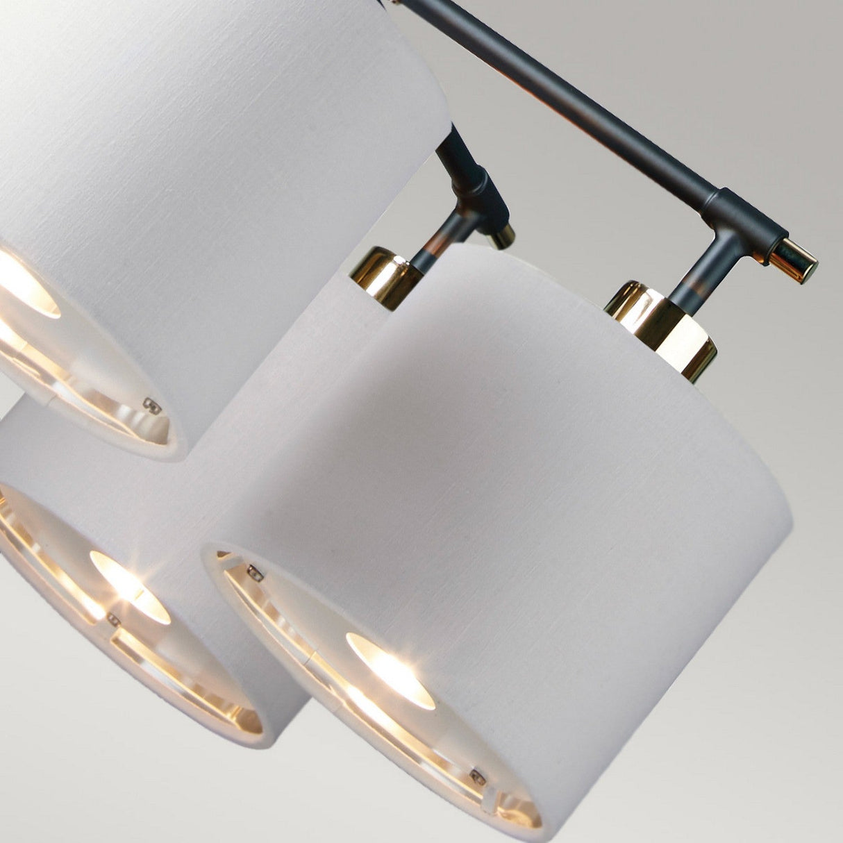 A close-up of the Balance 5 Light Chandelier showcases its three cylindrical white fabric lampshades elegantly connected to a black and polished nickel rod, offering an energy-efficient lighting solution with a sleek and contemporary appearance against a neutral background.