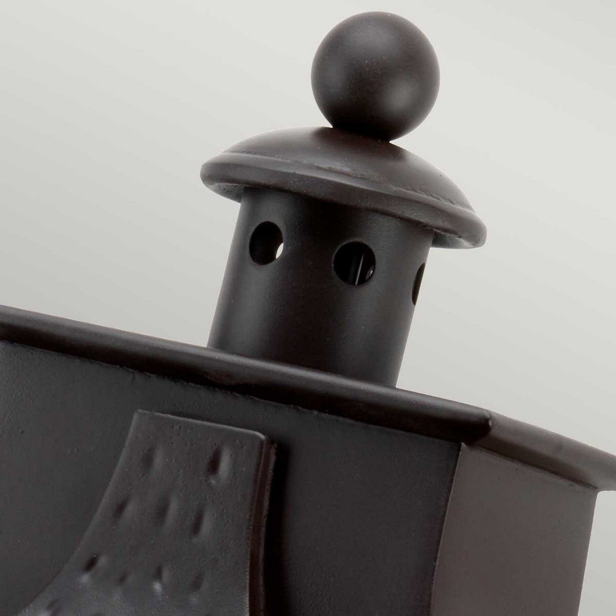 A close-up of the Balmoral 3 Light Outdoor Wall Lantern in Old Bronze reveals its black metal structure with a dome-shaped top and circular holes, reminiscent of outdoor wall lighting. The design boasts clean lines and a matte finish, exuding vintage charm.