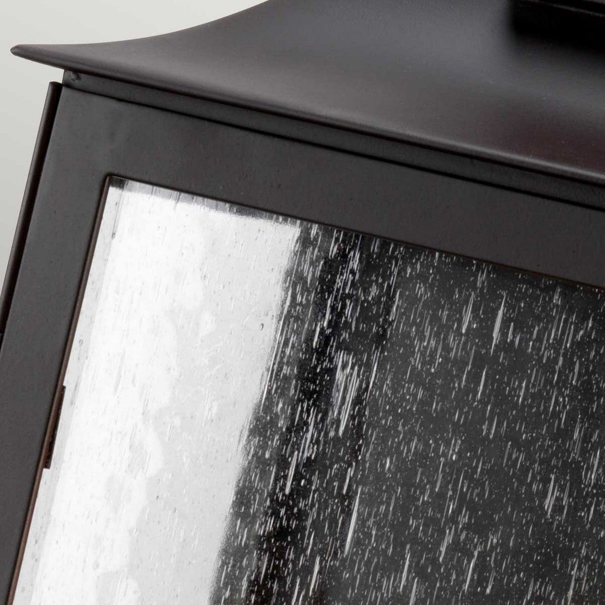 Close-up of a rain-soaked Balmoral 3 Light Outdoor Wall Lantern in old bronze, with raindrops streaming down its glass. The lantern's metal frame, exuding vintage charm, is beautifully highlighted by the texture and wetness of the surface.