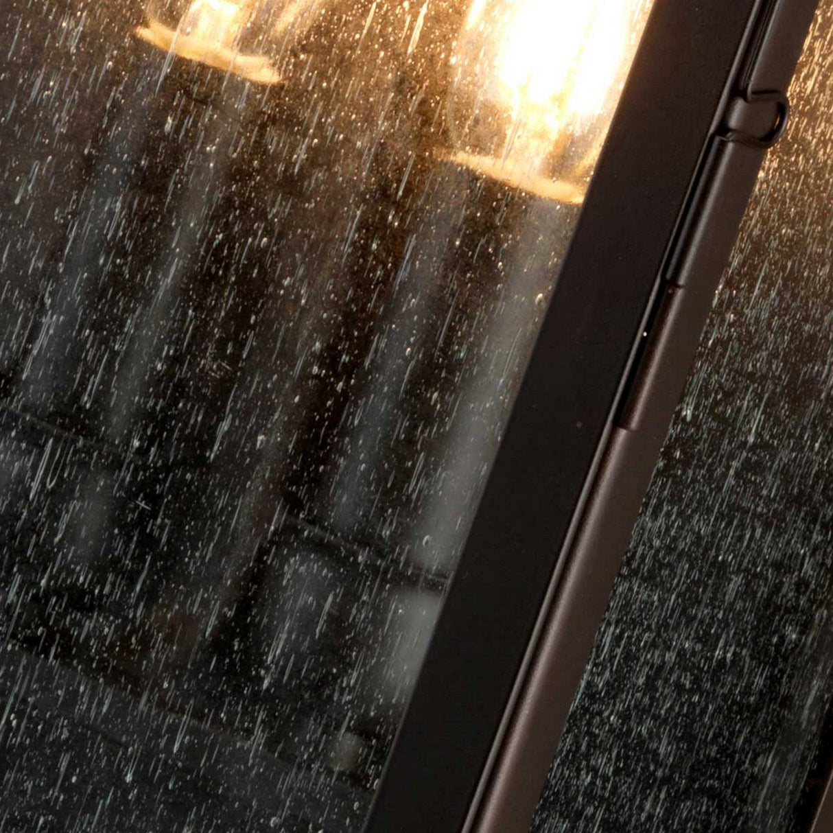 Rain droplets stream down a window, softly illuminated by the Balmoral 3 Light Outdoor Wall Lantern in the background, its old bronze finish adding a touch of vintage charm to create a cozy and serene atmosphere.