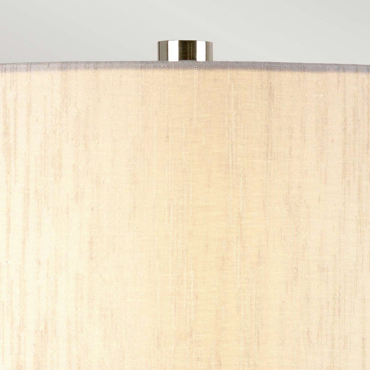 A close-up of the Barbican 1 Light Table Lamp showcases a graphite and silver shade with a smooth texture, resting on its ceramic base. The top is accented by a metallic finial, and the light casts a soft, warm glow on the material. This lamp elegantly combines style and function, adding charm to any room.