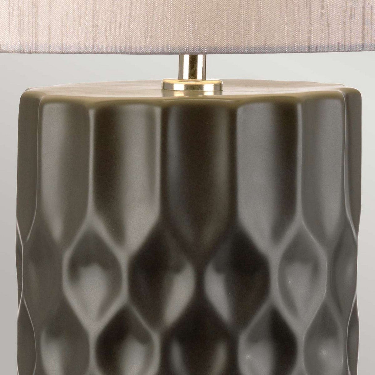 Close-up of the Barbican 1 Light Table Lamp, showcasing a ceramic base with a textured, geometric pattern in muted olive green. It is topped with a sleek, graphite and silver lampshade. The style is modern and minimalist.