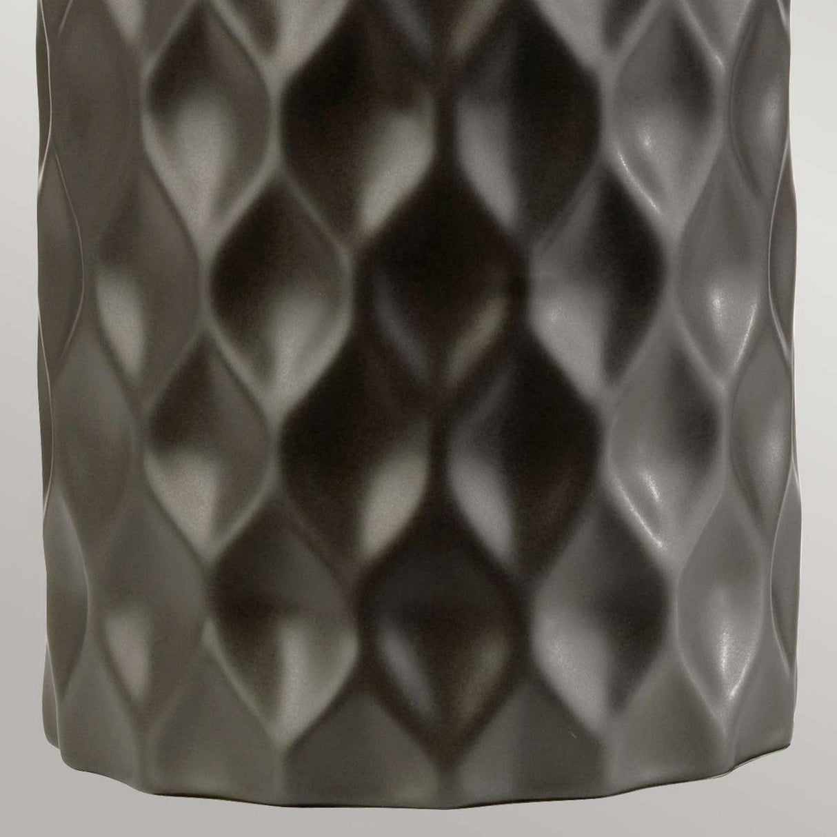 Close-up of a textured surface with a diamond or rhombus pattern resembling the silver shade of the Barbican 1 Light Table Lamp in Graphite. The surface exhibits a metallic appearance, reflecting light with an uneven, wavy texture and featuring a dark gray color.