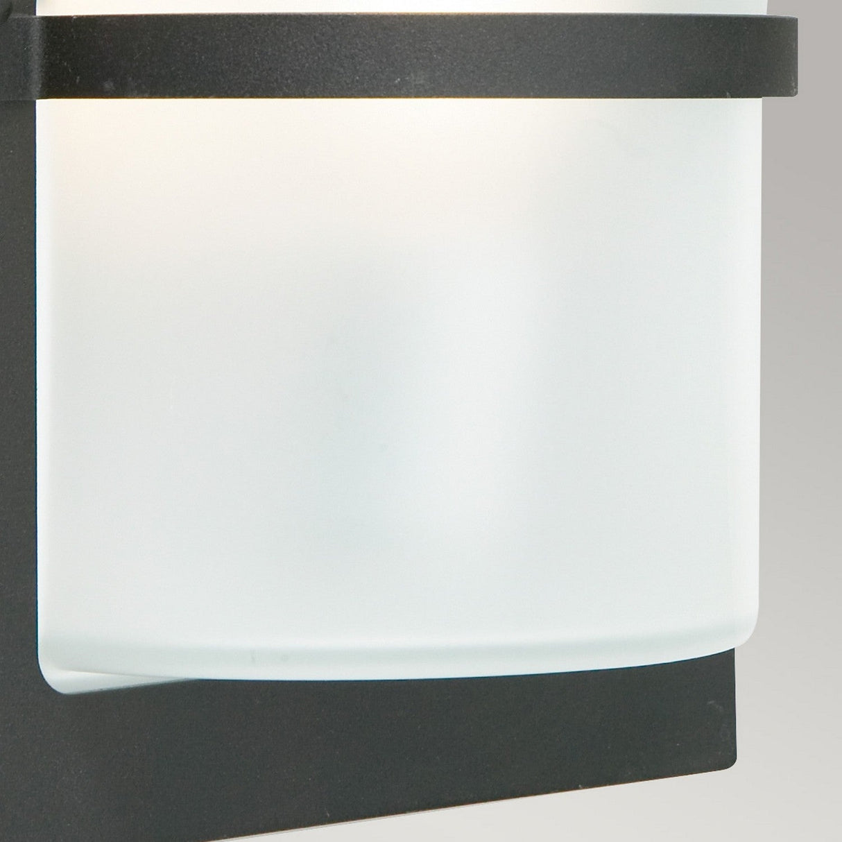 Presenting the Basel Outdoor 1 Light Wall Lantern - Black With Frosted Glass, a contemporary lighting fixture featuring a streamlined design. Its frosted glass cylindrical shade and black base integrate effortlessly into any environment. Boasting an IP54 rating, it provides a gentle, diffused illumination against a plain gray backdrop.
