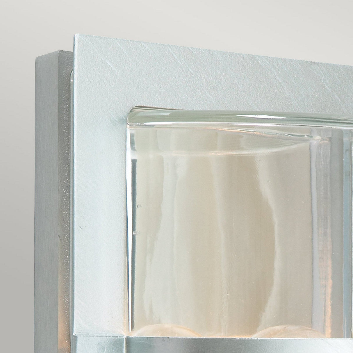 Detailed view of the Basel Outdoor 1 Light Wall Lantern in a sleek, metallic design. This fixture boasts clear glass and minimalist styling with clean lines and a subtle silver finish that enhances its neutral aesthetic.