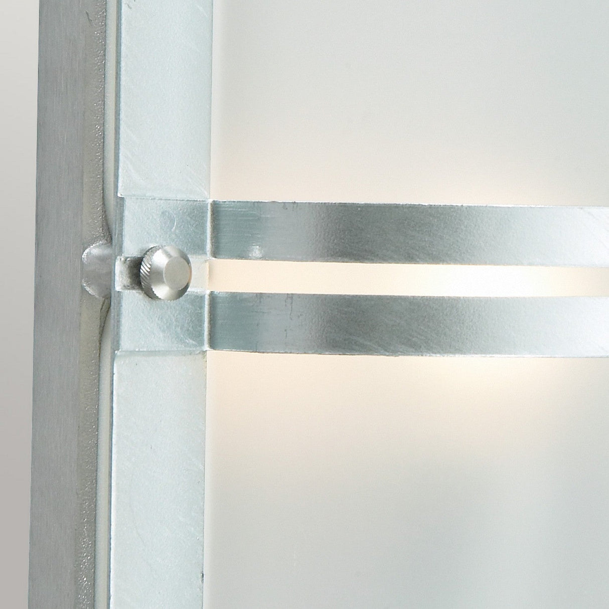 Close-up of the Basel Outdoor 1 Light Wall Lantern in silver, designed with a frosted glass panel and sleek metal structure. Its cylindrical support provides warm ambient lighting and boasts an IP54 rating, offering a contemporary and minimalistic appearance.