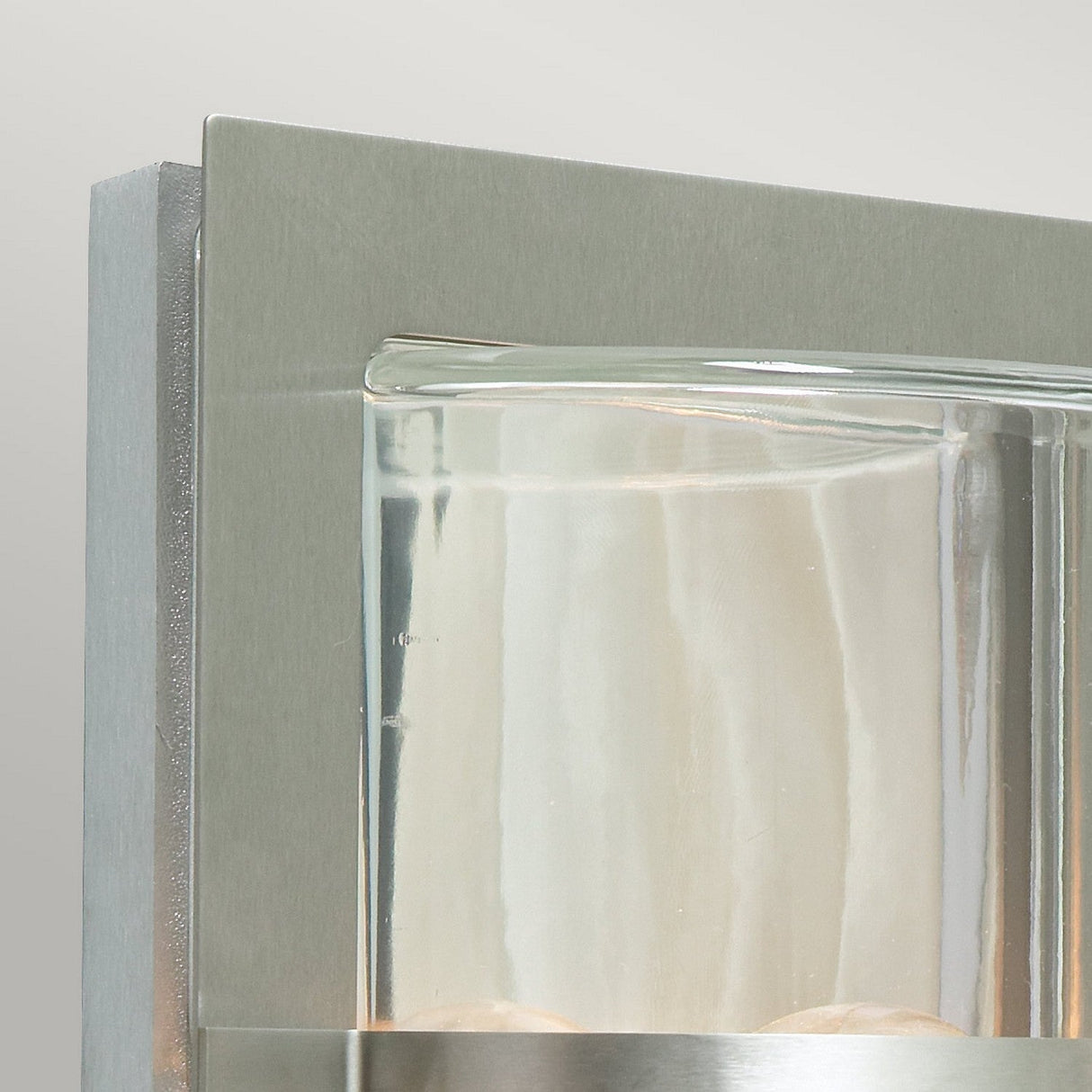 Close-up of the Basel Outdoor 1 Light Wall Lantern, showcasing its sleek rectangular stainless steel base and clear glass shade. The light emits a subtle, warm glow, offering a minimalist and contemporary design reminiscent of an elegant outdoor wall lantern.