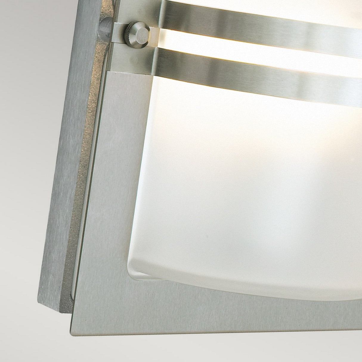 Close-up of the Basel Outdoor 1 Light Wall Lantern - Stainless Steel With Frosted Glass, featuring a modern design. Its brushed metal and horizontal stainless steel accents complement the minimalist silver-gray color scheme, creating an elegant and contemporary look.
