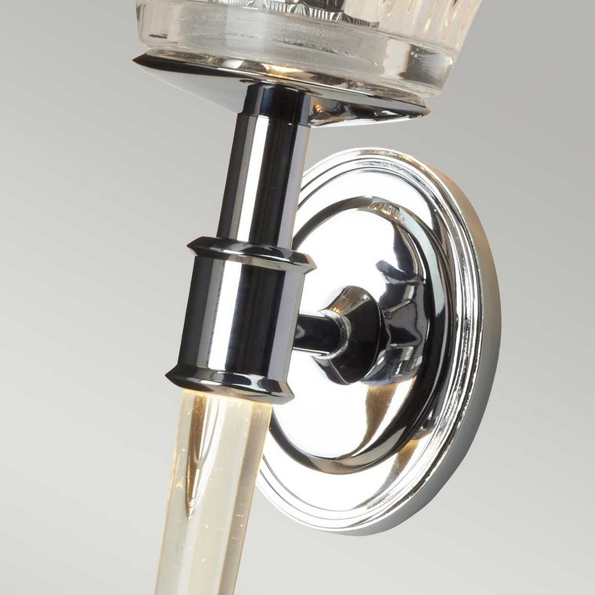 Close-up of the Agatha 2 Light Wall Light in polished chrome, featuring clear-cut glass shades. The fixture has a circular base with a sleek, reflective design and a decorative horizontal ring detail on the vertical stem. The light is off, highlighting its elegant, modern style.