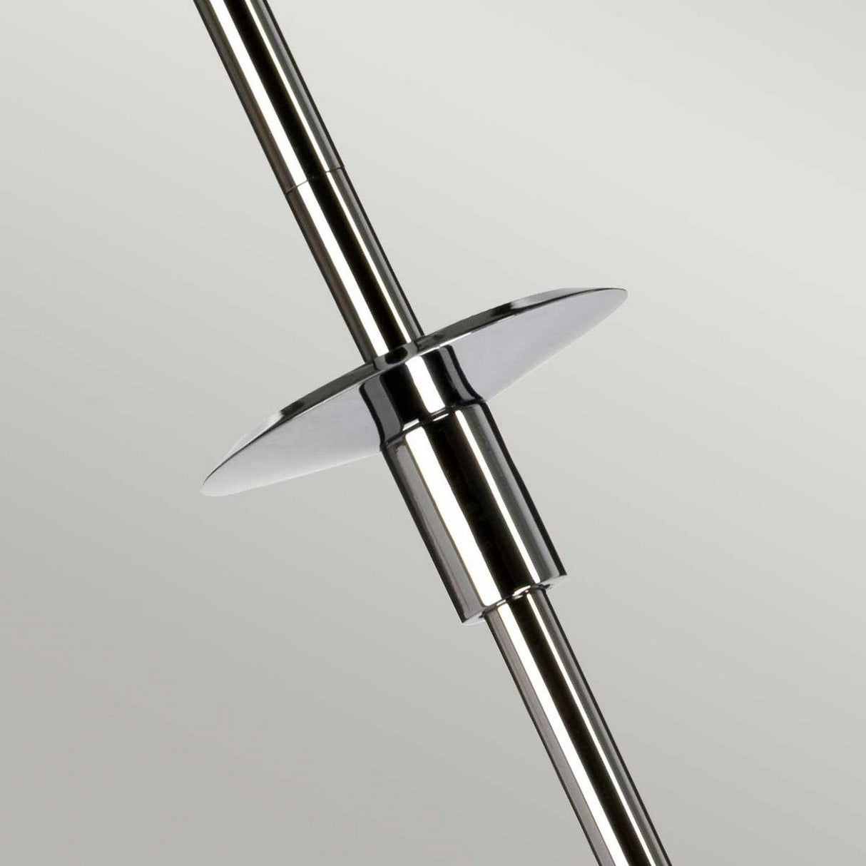 A close-up of the Agatha 1 Light Pendant in polished chrome reveals a circular disc attached perpendicularly to its shiny surface, set against a plain light gray background. The rod's reflective finish catches the light, emphasizing its metallic texture reminiscent of sleek bathroom lighting.