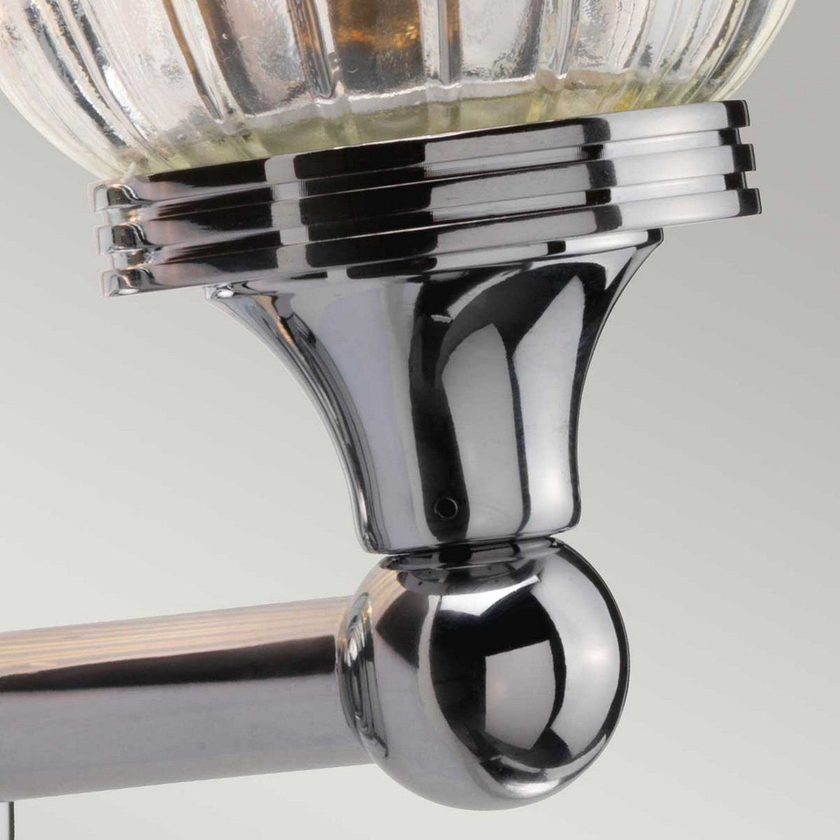 Close-up of the Austen-1 Wall Light - Polished Chrome showcasing its polished chrome finish and ribbed glass globe, accented by shiny metal detailing. The light fixture features a spherical base connected to a horizontal metal support, all set against a neutral background.