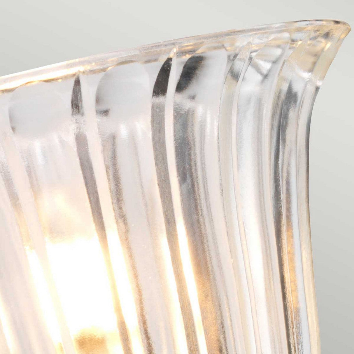 Close-up of a translucent, fluted glass shade with vertical ridges, illuminated from within by a warm light. The Austen-1 Wall Light's polished chrome base complements the glowing effect, accentuating the textured patterns in the glass for an elegant finish.