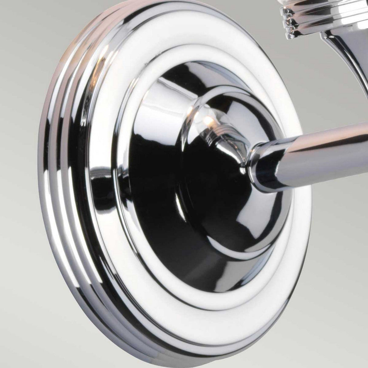 Close-up of the Austen-2 Wall Light in polished chrome, showcasing a circular wall mount with a reflective surface and concentric design elements. This fixture is crafted to accommodate an LED G9 bulb, connected to a tubular structure that extends outward against a plain background.