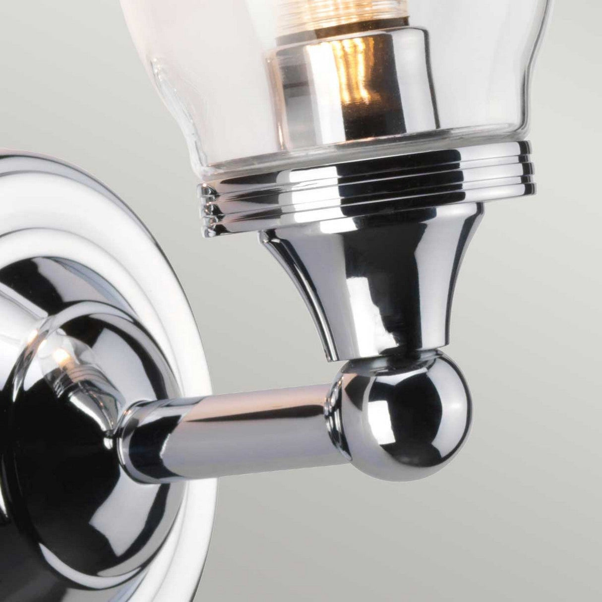 Close-up of the Austen-2 Wall Light in polished chrome, featuring a clear glass shade. The illuminated LED G9 bulb emits a warm glow, enhancing the fixture's sleek and modern design.