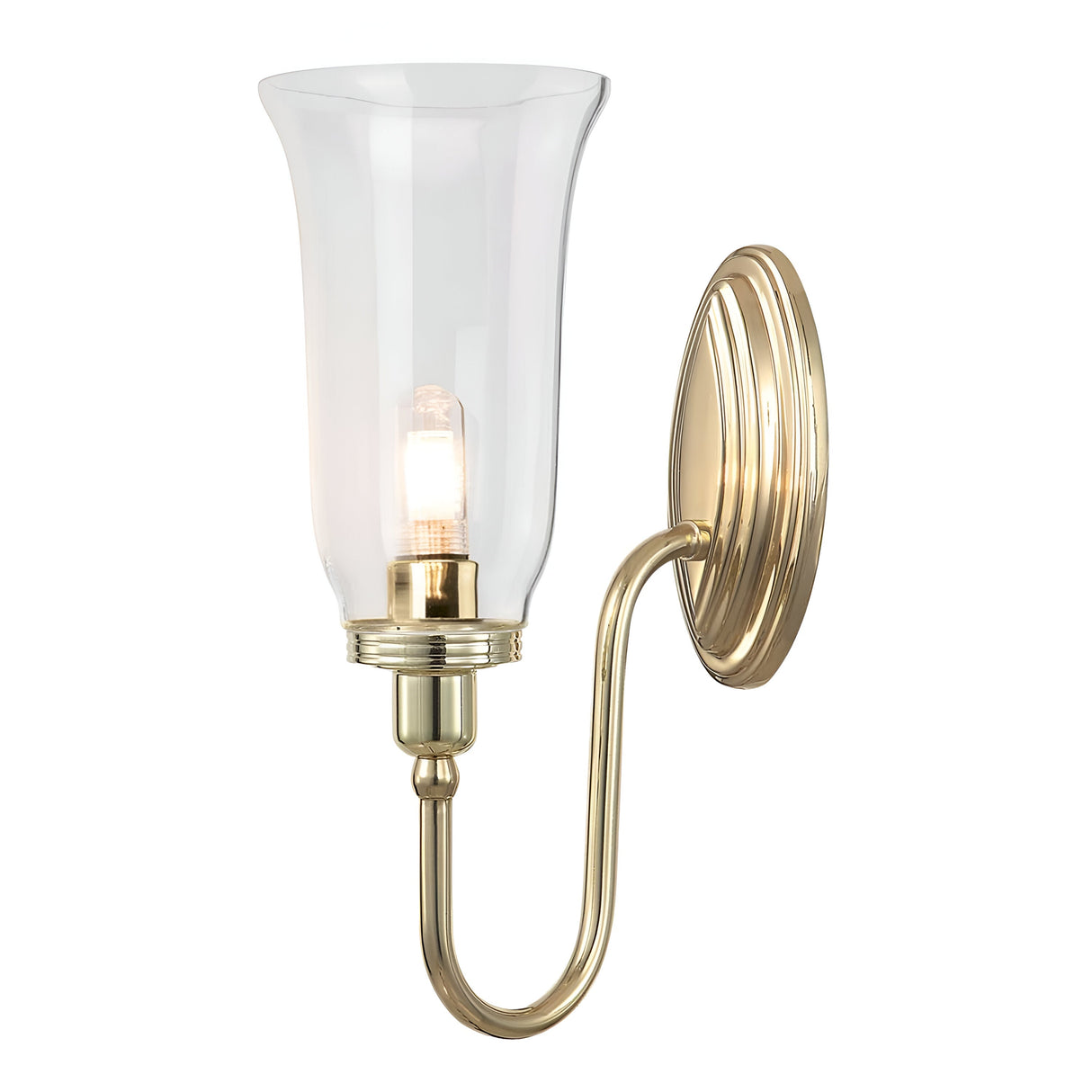 The Blake Wall Light - Polished Brass boasts a graceful design with a curved arm linking the circular wall mount to an elegantly flared glass shade. It includes an LED G9 lamp inside, which emits a cozy glow, enhancing the timeless charm of this sophisticated fixture.
