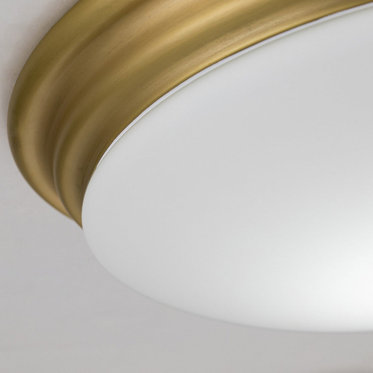 Close-up of the Brompton Flush Light - Brushed Brass, showcasing a white frosted glass dome bordered by a brushed brass rim, mounted on a white ceiling, exuding Art Deco elegance.