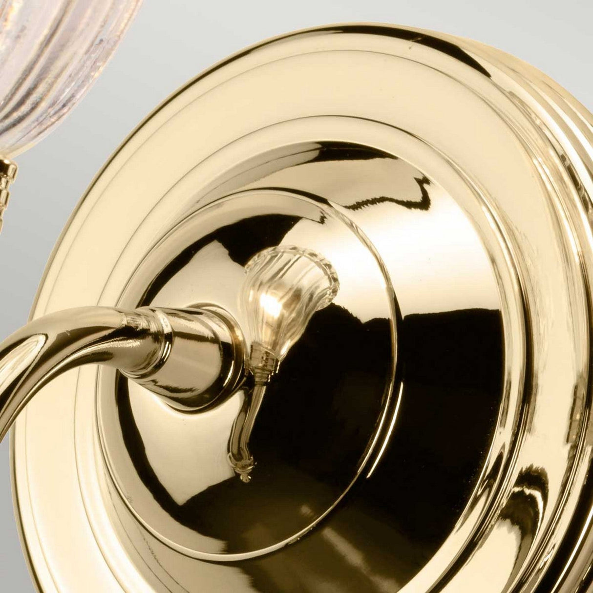 Close-up of the Carroll Wall Light - Polished Brass, featuring a curved arm and a clear bulb. The polished brass surface reflects light, offering a sleek and modern touch ideal for vintage-inspired bathroom vanity lighting.