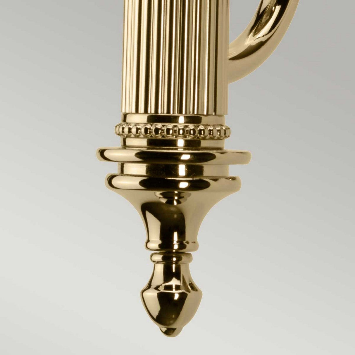 Close-up of the Carroll Wall Light - Polished Brass, showcasing its vintage-inspired design with an ornate, gold-colored metal fixture. It features a ribbed cylindrical body and decorative beading, extending into a tapered end that beautifully reflects light off its gleaming surface.