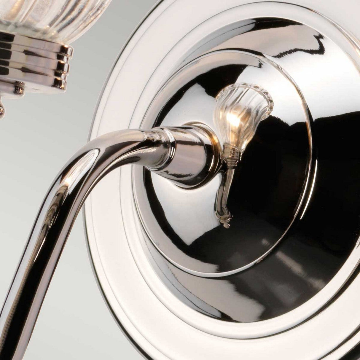 A close-up of the Carroll Wall Light - Polished Nickel showcases its curved arm and small decorative light bulb, reflecting ambient light off its shiny, metallic finish.