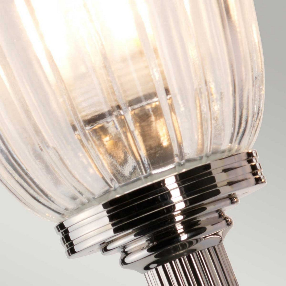 Close-up of the Carroll Wall Light - Polished Nickel, showcasing its ribbed glass shade and gleaming polished nickel base, softly lit against a light gray background.