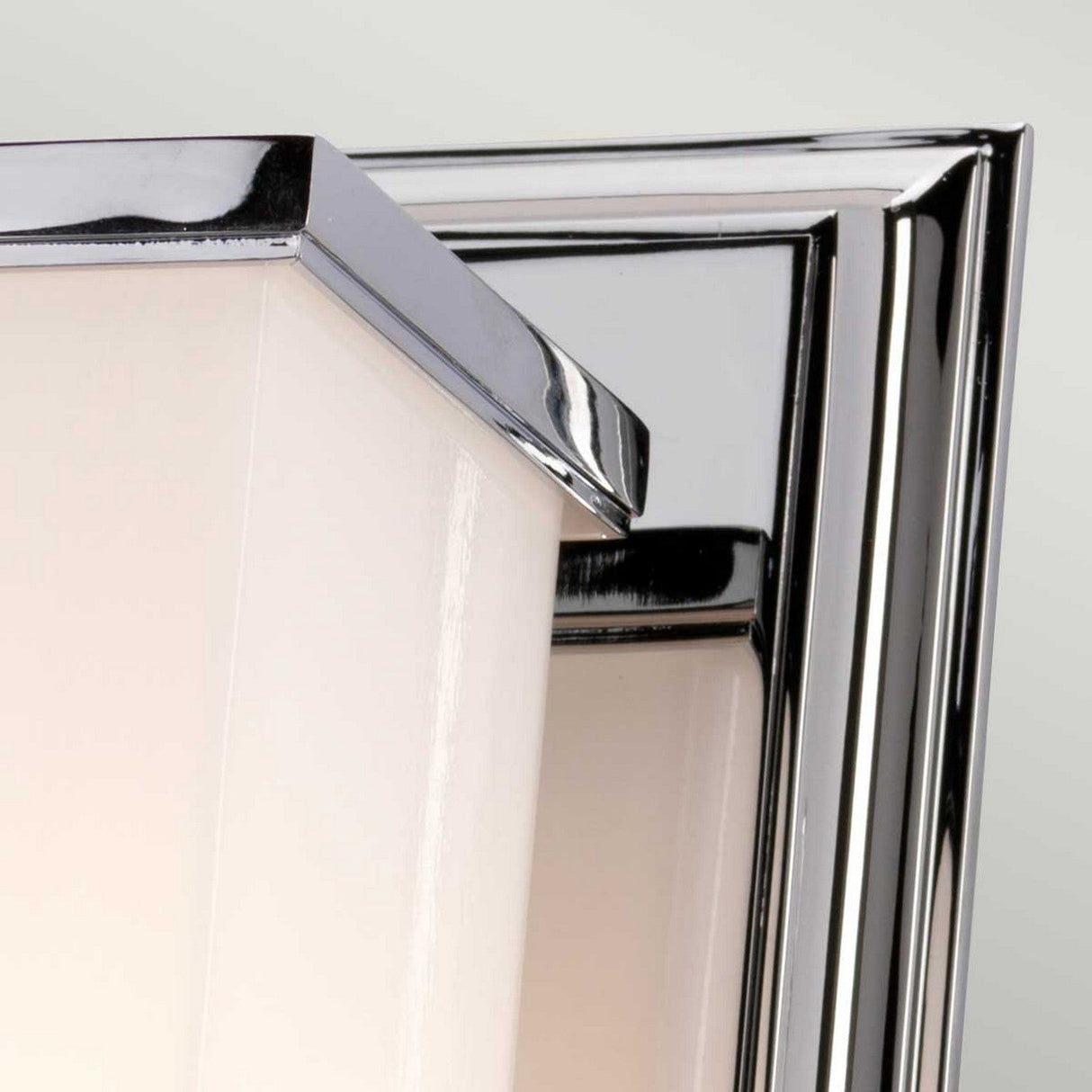 Close-up of the Cambridge Wall Light - Polished Chrome, showcasing an opal glass shade and a polished chrome frame. The design exhibits clean lines and a sleek, contemporary appearance, set against a neutral background.